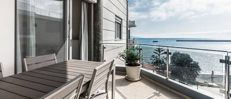 A balcony with a table and chairs, a potted plant, and a view of the sea.