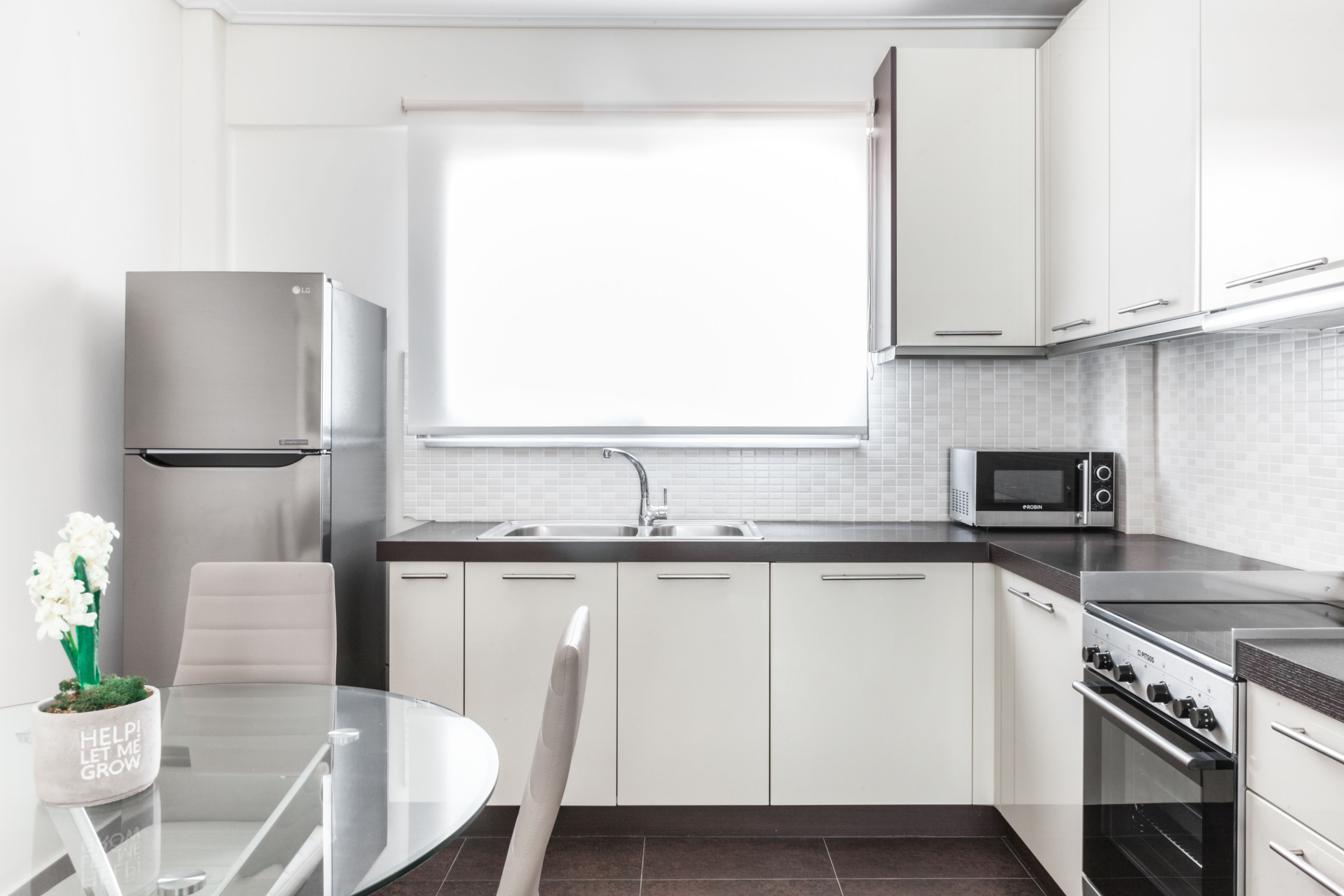 A modern kitchen with white cabinets, a stainless steel refrigerator, a microwave, a stove, and a window providing natural light.