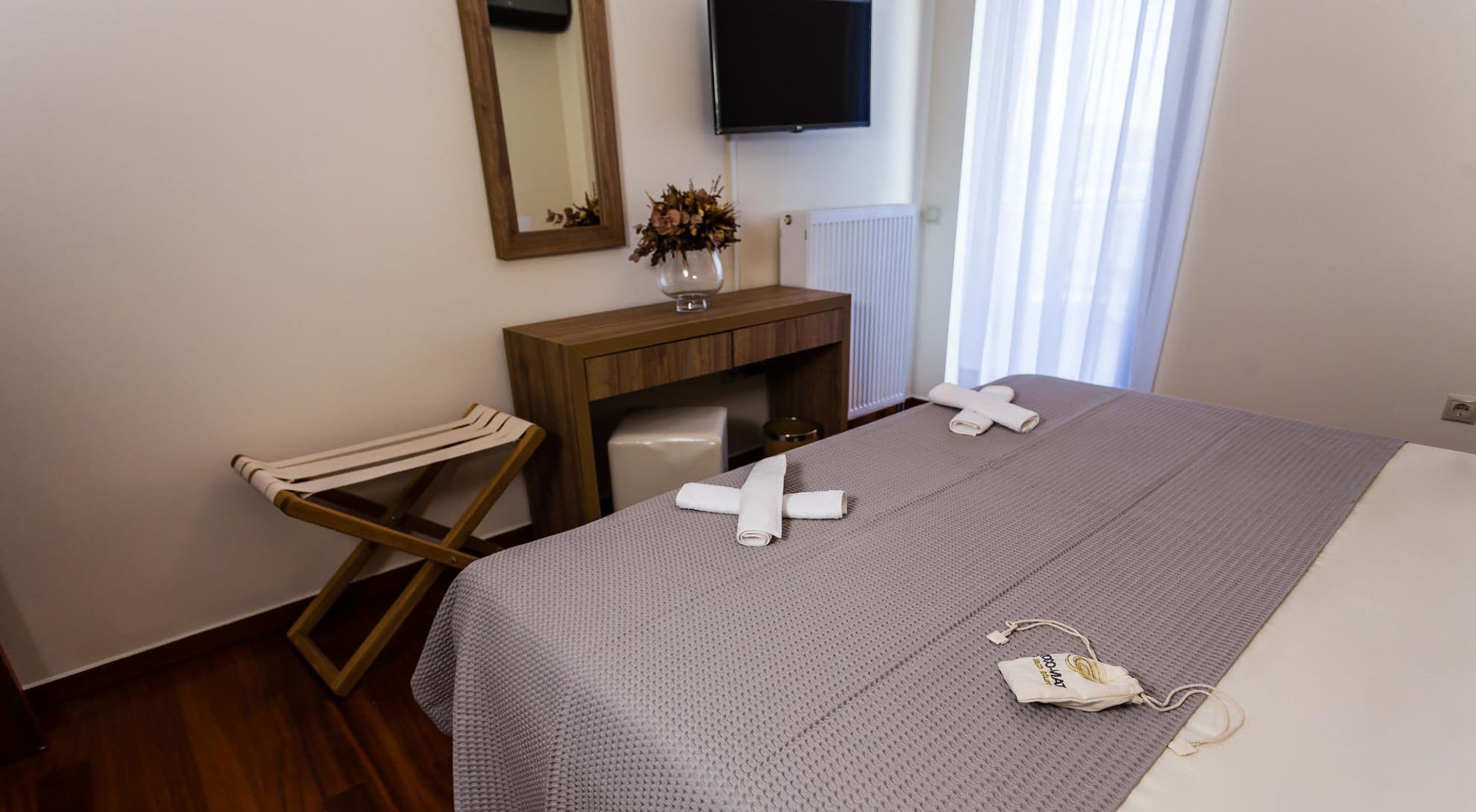 A hotel room with a bed, a wooden desk, a chair, a mirror, a TV, and a window with curtains.