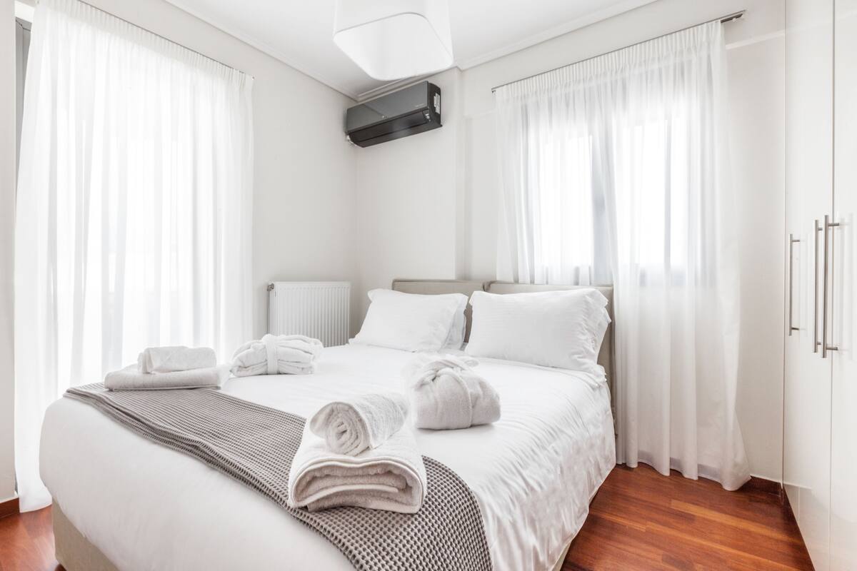A modern hotel room with a large bed, white linens, and a neatly made bed with towels.