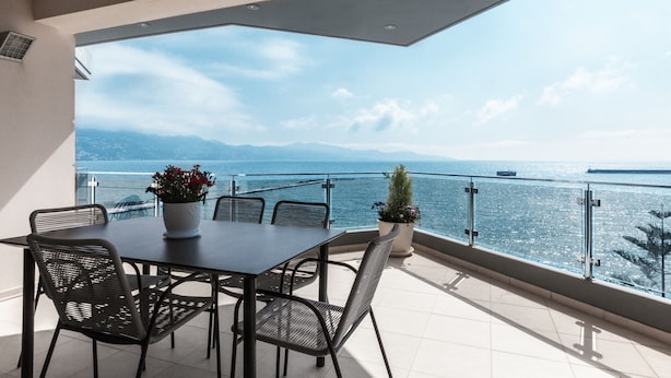 Ein Balkon mit Tisch und Stühlen, mit Blick auf ein Gewässer und ferne Berge.