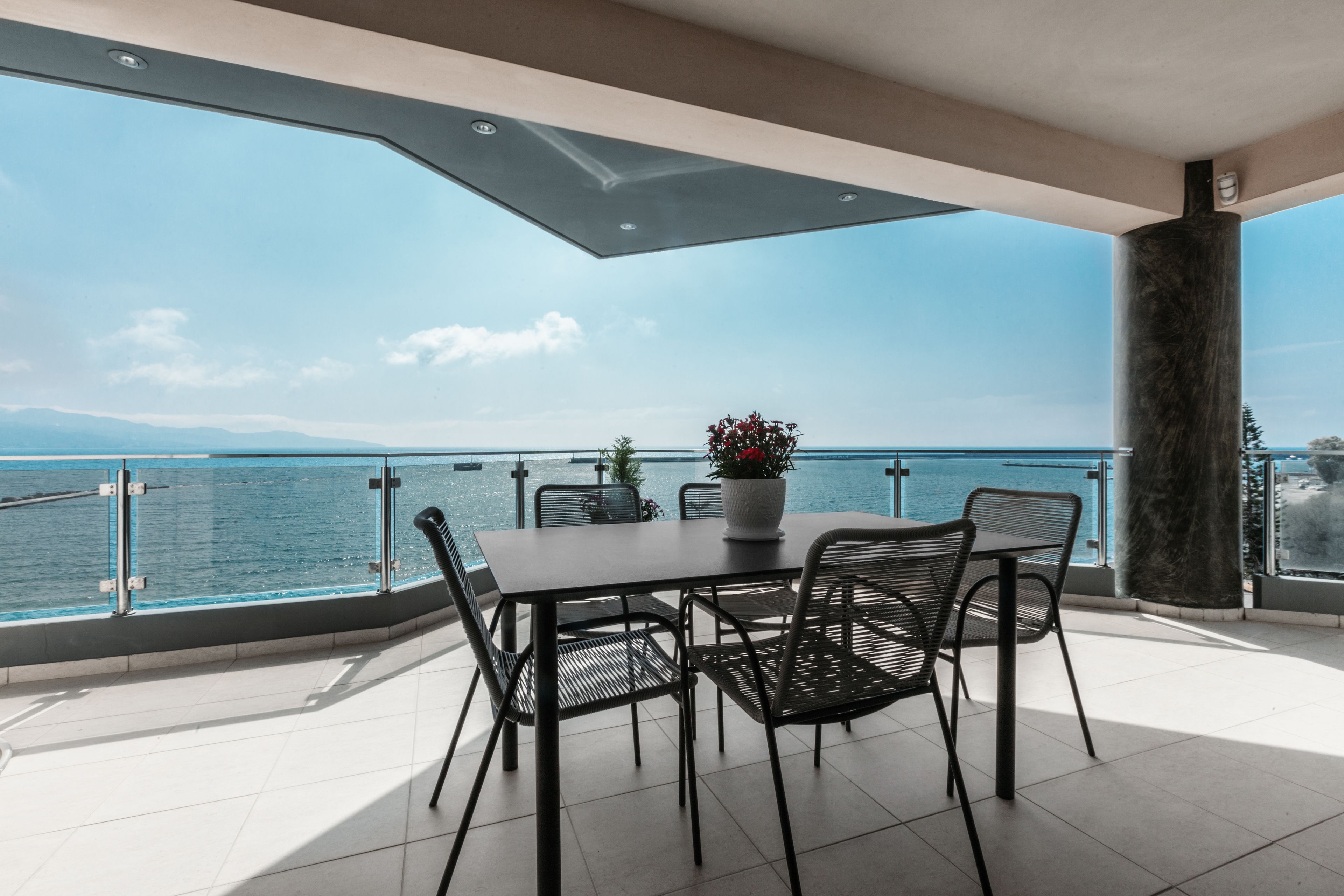 A terrace with a table and chairs, a potted plant, and a view of the sea.