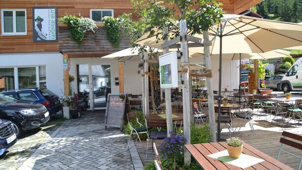 An outdoor seating area with wooden tables and chairs, umbrellas, and potted plants. - Bergsteiger-Hotel Grüner Hut (Bad Hindelang)