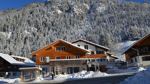 A modern chalet-style building with a wooden facade, situated in a snowy mountain village with a backdrop of snow-covered trees and a mountain. - Bergsteiger-Hotel Grüner Hut (Bad Hindelang)