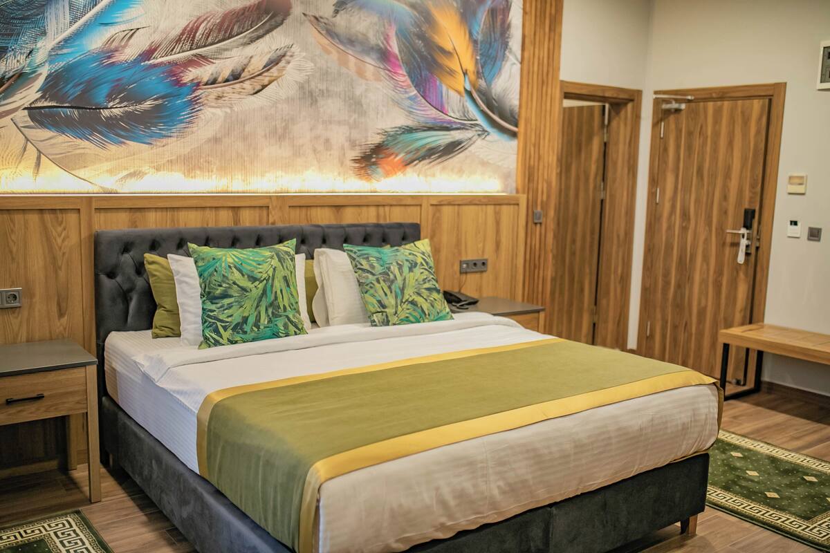 Une chambre à coucher bien aménagée, avec un grand lit, une tête de lit en bois et une peinture abstraite aux couleurs vives accrochée au-dessus du lit.