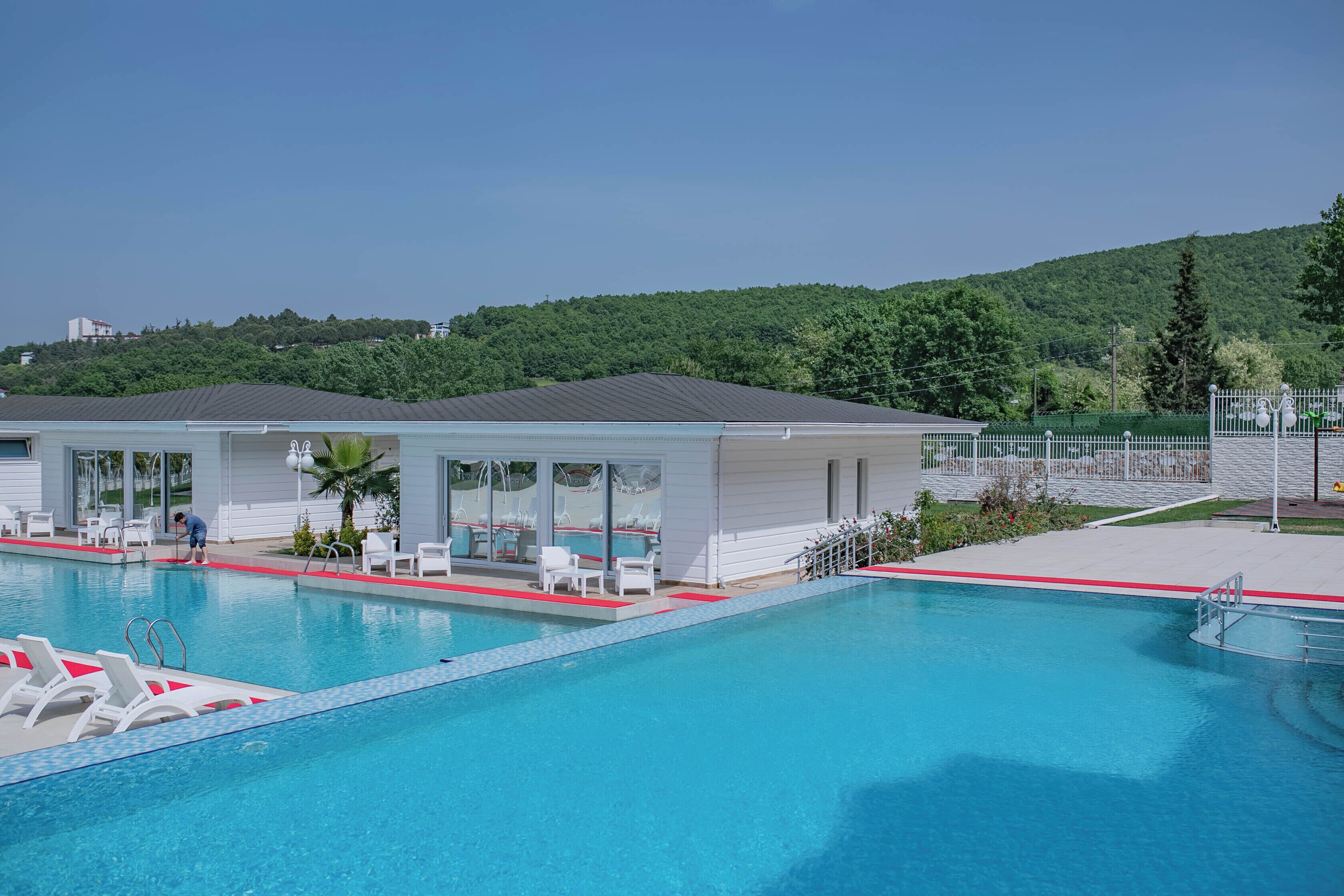 A swimming pool with lounge chairs and a covered area with glass doors.
