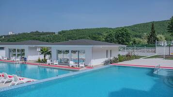 A swimming pool with lounge chairs and a covered area with glass doors.