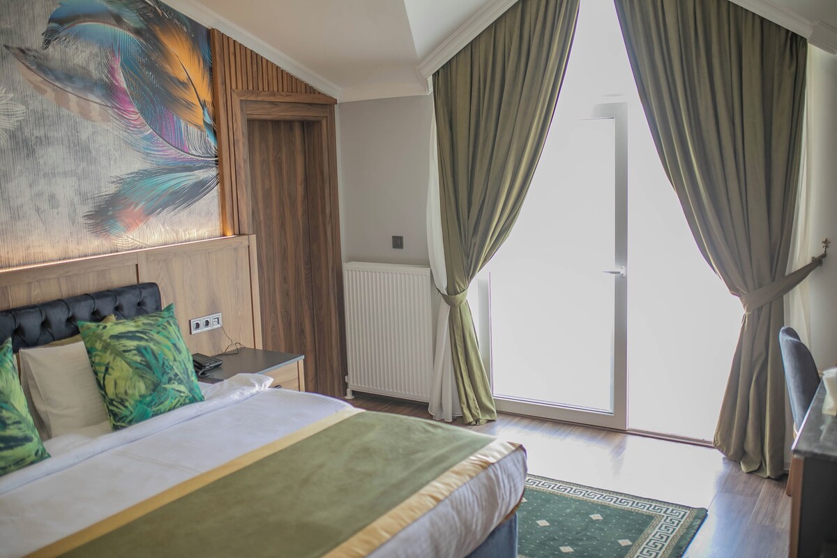 Een hotelkamer met een bed, een bureau, een stoel, een schilderij aan de muur en uitzicht op het omliggende landschap.