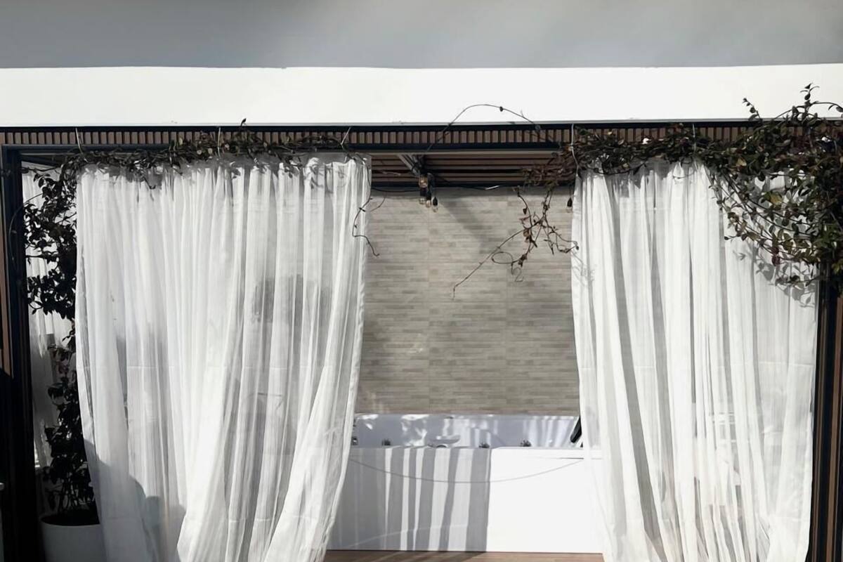 Un espace extérieur abrité, agrémenté de rideaux blancs et doté d’un plancher en bois.