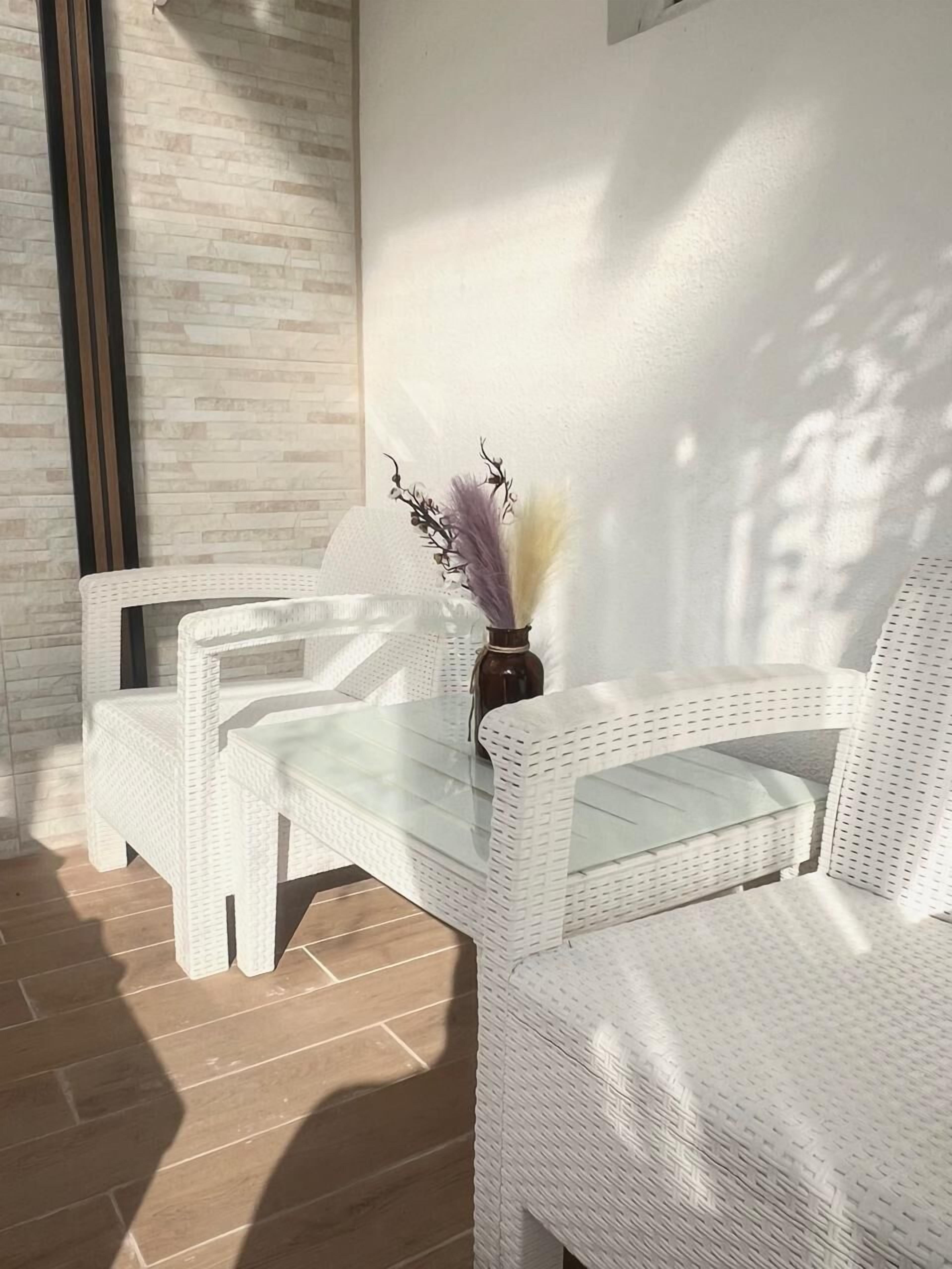 A sunlit room with wicker furniture and a glass table, featuring a vase with dried flowers.
