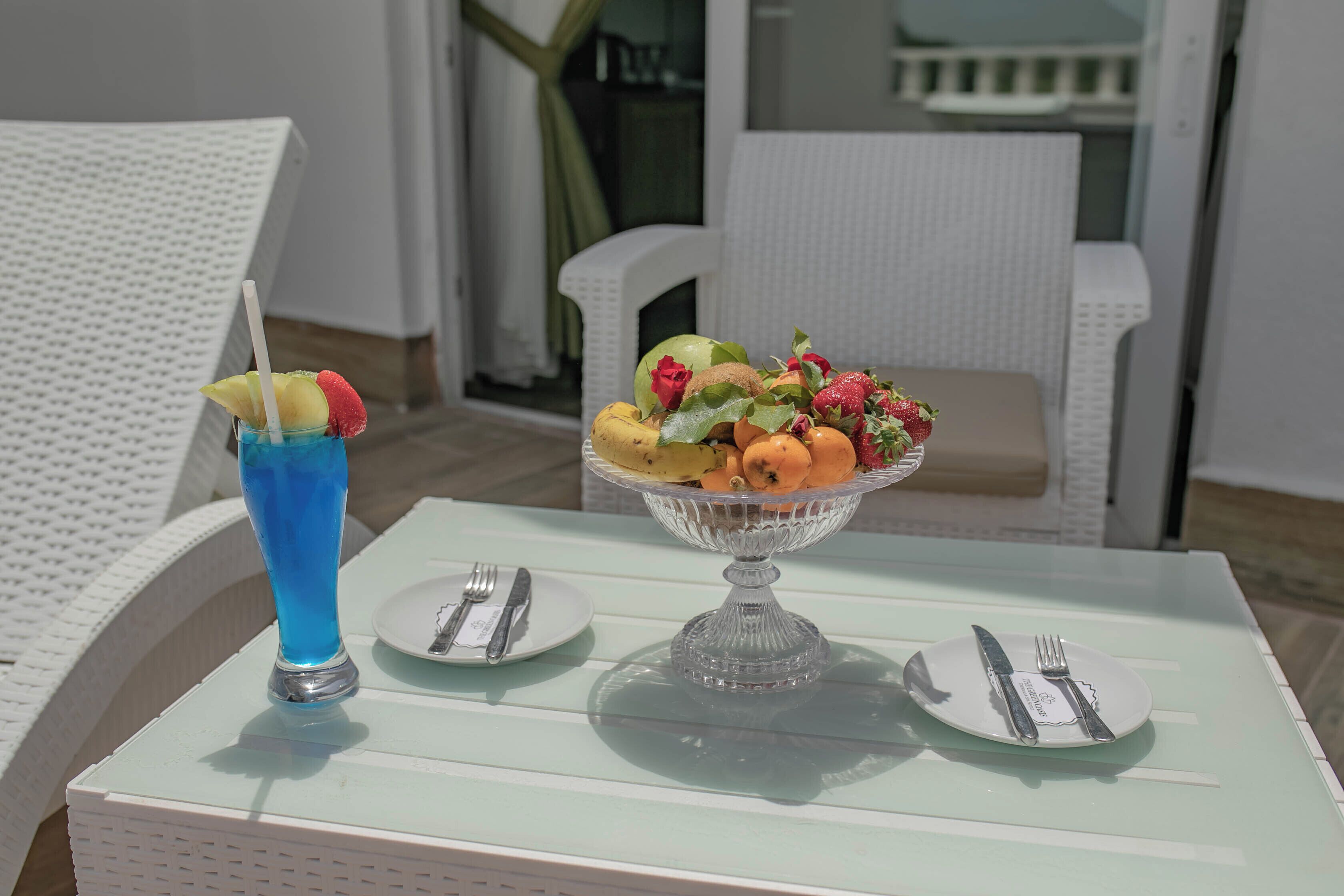 A dining table with a fruit bowl and a blue drink on a white tablecloth.