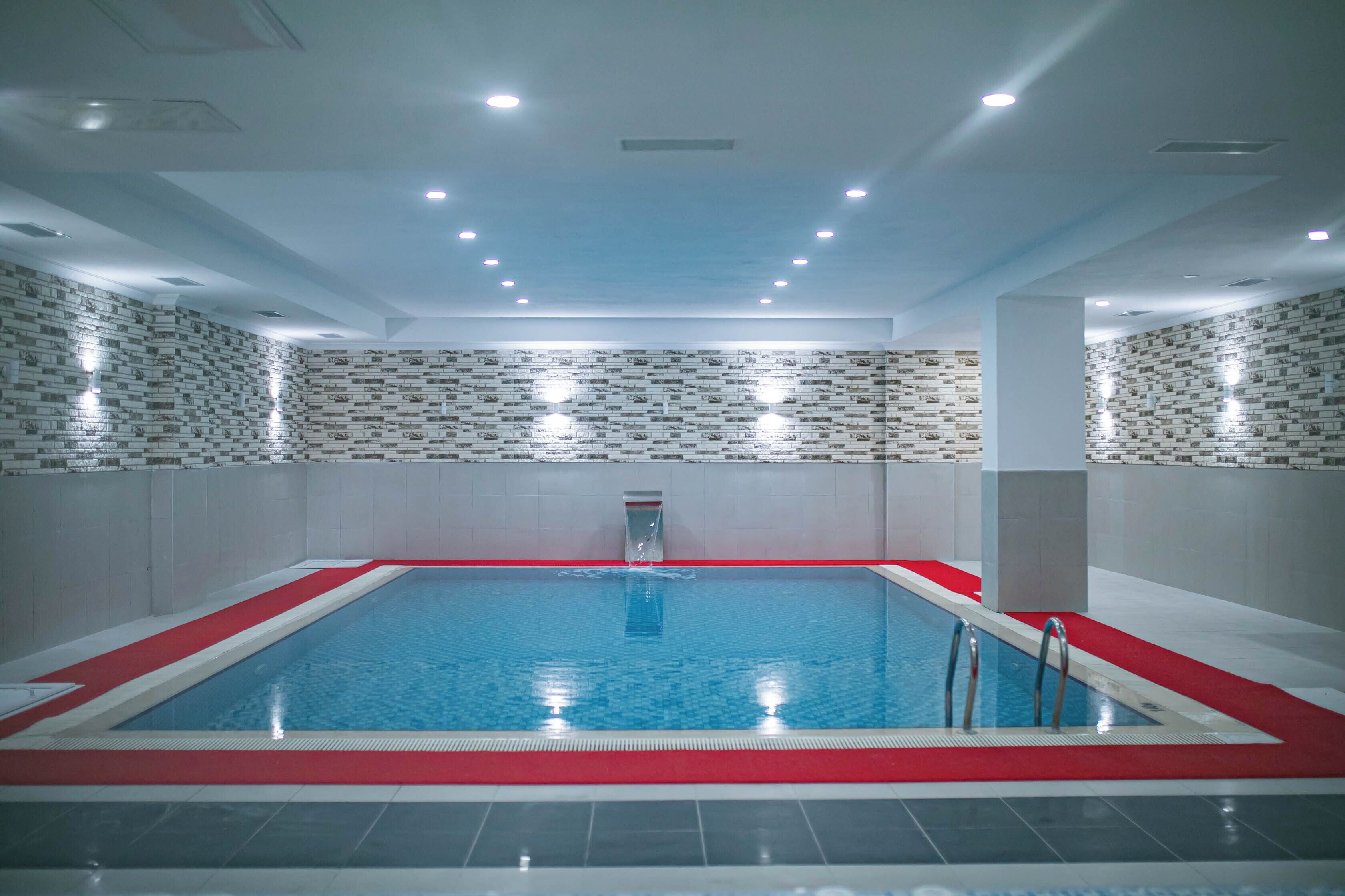 Una piscina interior con borde rojo, paredes de azulejos e iluminación en el techo.