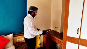 A person cleaning a wooden counter in a room with a blue wall and a white door. - Celebrations Inn (Pune)