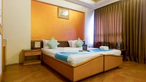 A hotel room with a large bed, wooden headboard, a nightstand, a bedside table, a water bottle, and a framed picture on the wall. - Celebrations Inn (Pune)