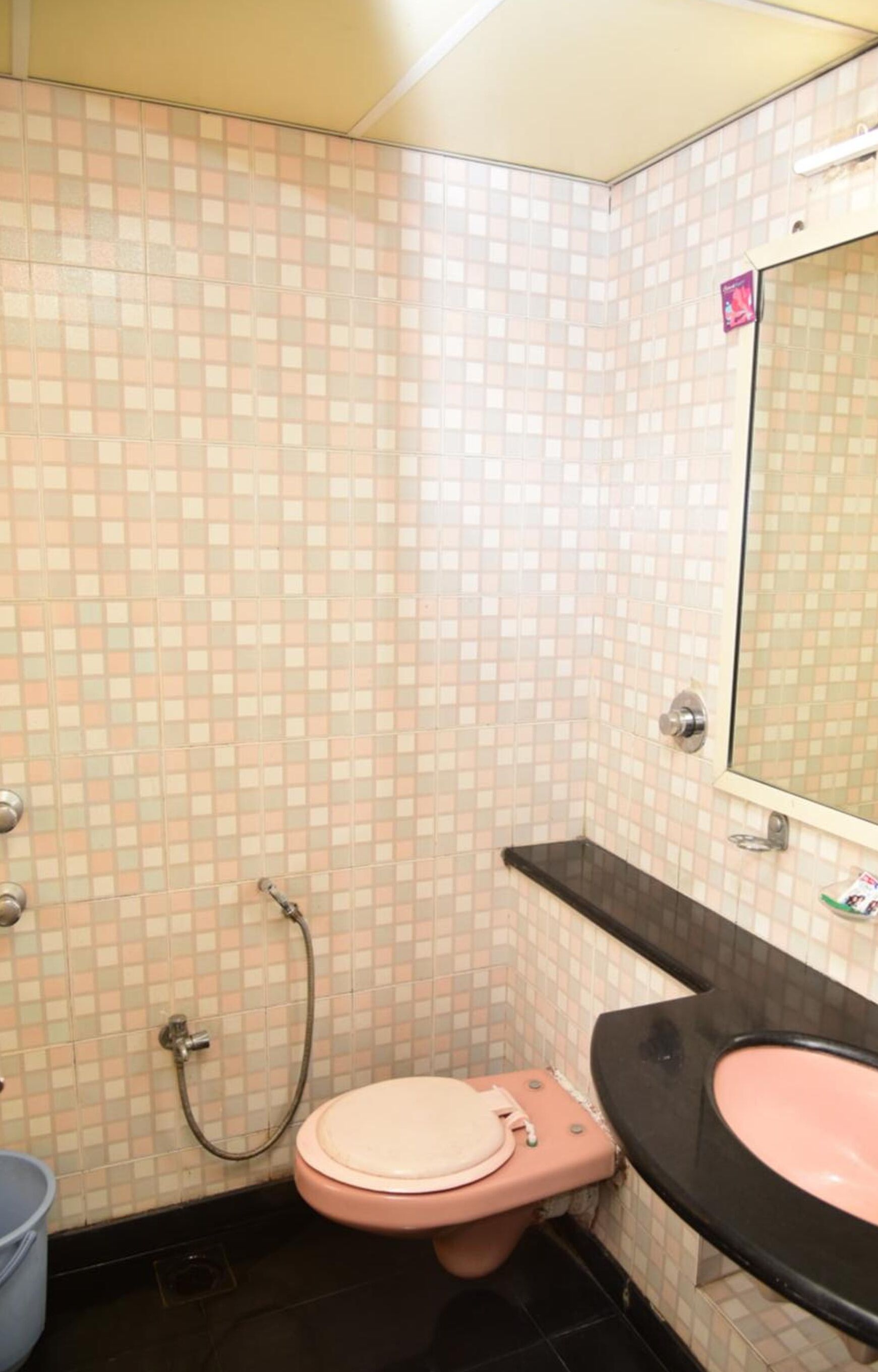 Une salle de bain avec des toilettes roses, un lavabo noir et un mur recouvert de carreaux.