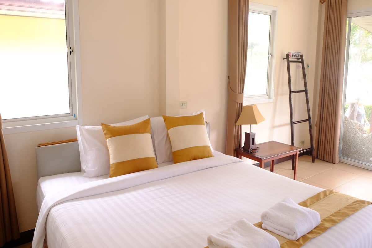 Habitación de hotel con una cama grande, dos almohadas, una mesita de noche, una lámpara y un ventanal con cortinas.