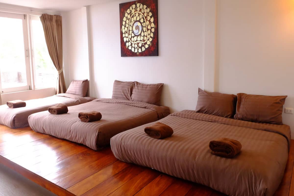 Habitación de hotel con dos camas, cada una con ropa de cama y almohadas marrones, piso de madera, una ventana con cortinas y una obra de arte colgada en la pared.