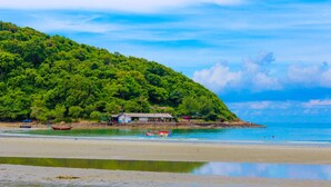 A beach with a house on a hill, calm water, and clear skies. - Fah Talay Resort (Rayong)