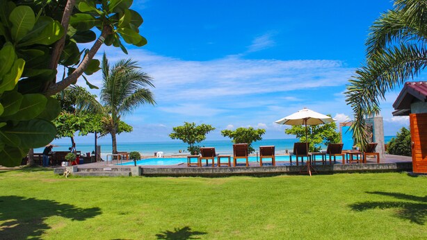 A poolside area with lounge chairs and umbrellas, a clear view of the ocean, and a grassy lawn. - Fah Talay Resort (Rayong)