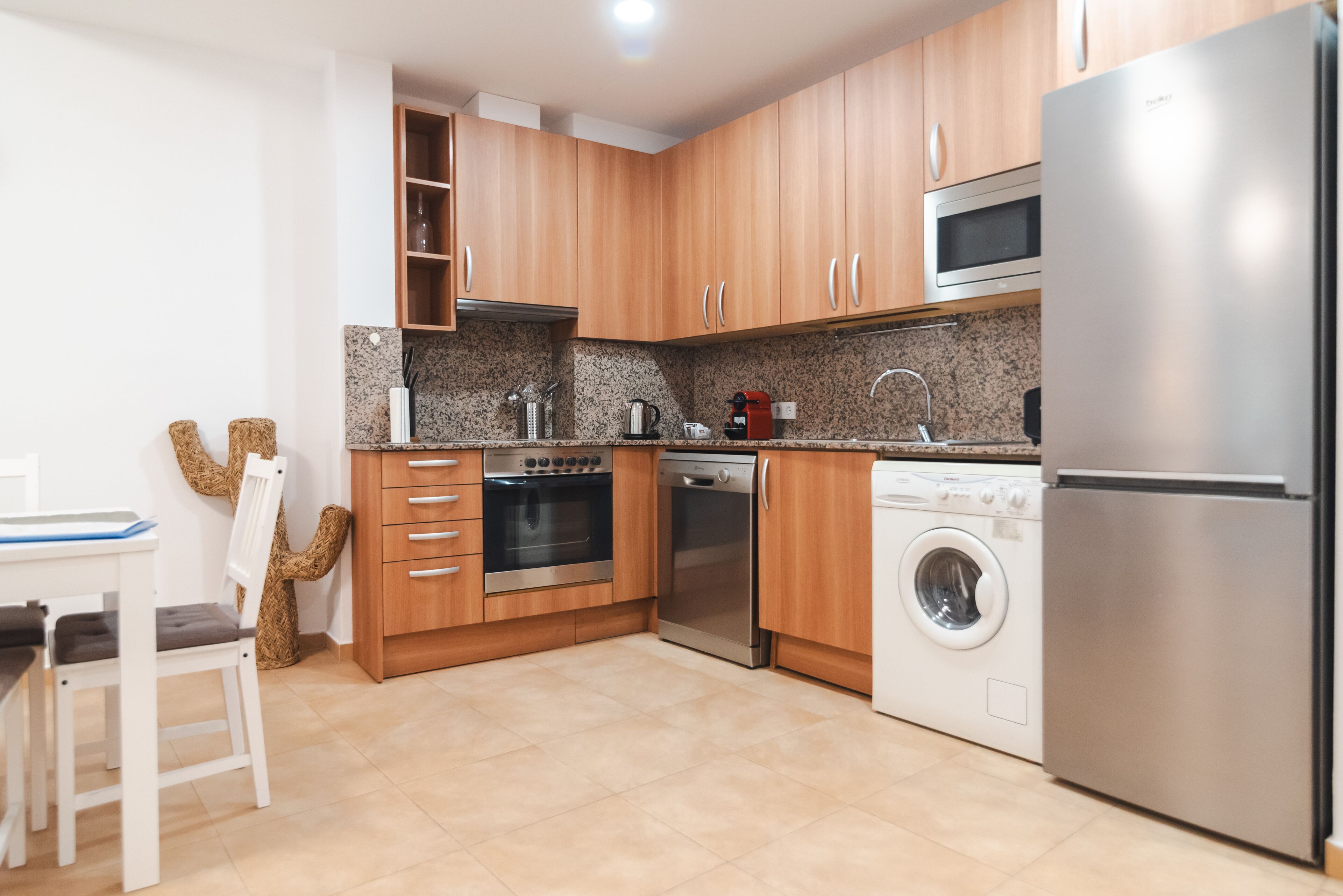 A modern kitchen with wooden cabinets, stainless steel appliances, a microwave, oven, dishwasher, and a washing machine.