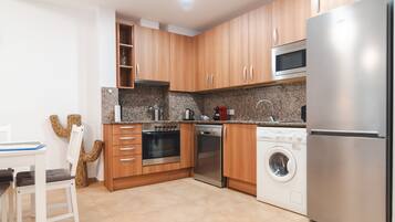 A modern kitchen with wooden cabinets, stainless steel appliances, a microwave, oven, dishwasher, and a washing machine.