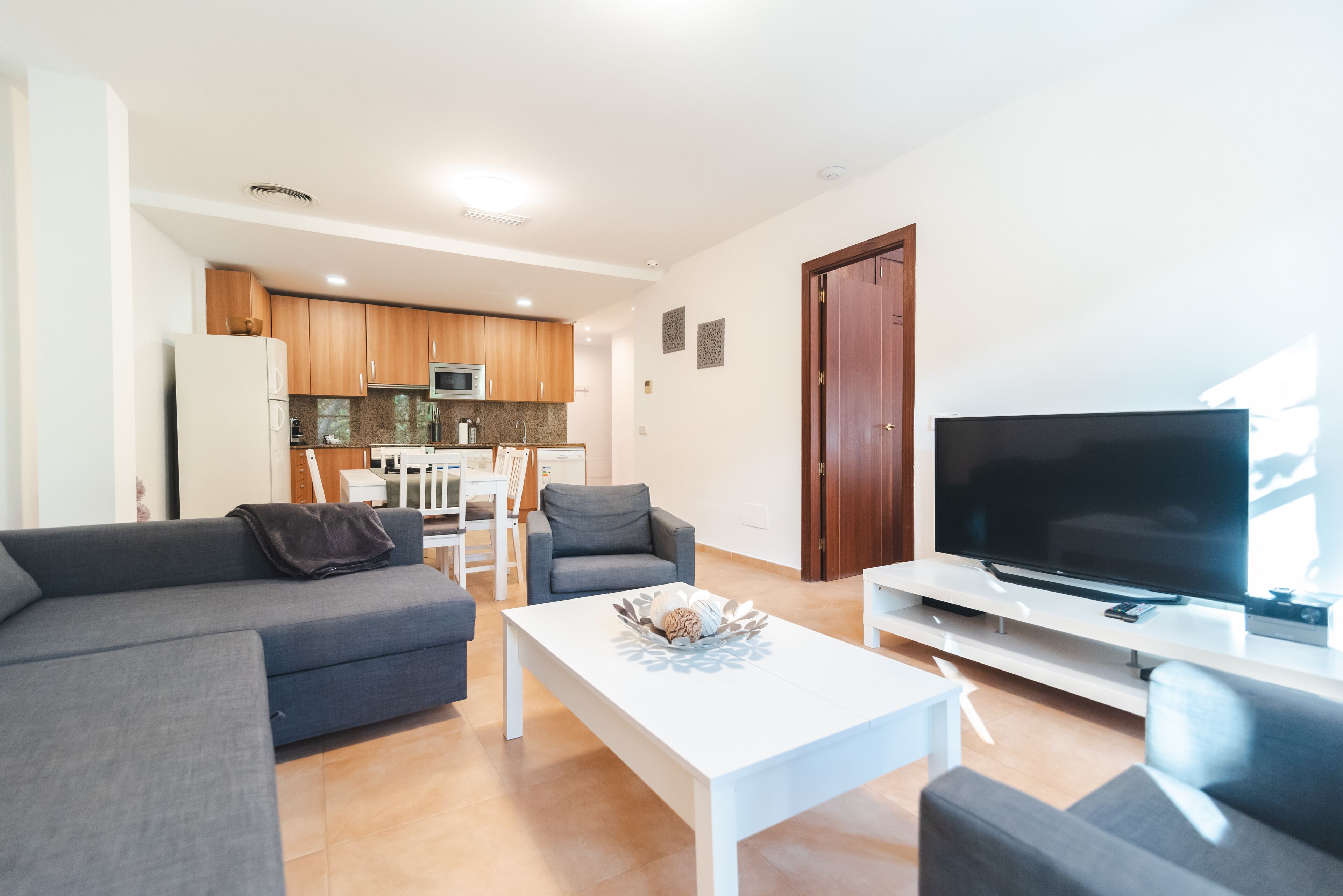 Uma sala de estar moderna com um sofá cinza, uma mesa de centro branca e uma televisão de tela plana.
