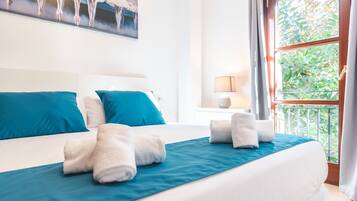 A hotel room with a large bed, blue bedding, white pillows, and a view of greenery through the window.