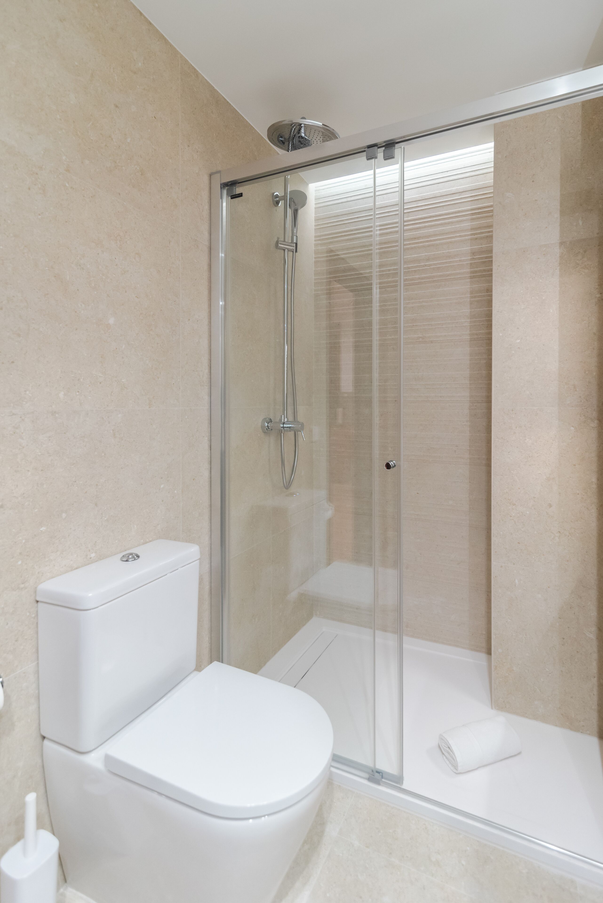 A modern bathroom with a glass-enclosed shower, a white toilet, and a towel on the floor.
