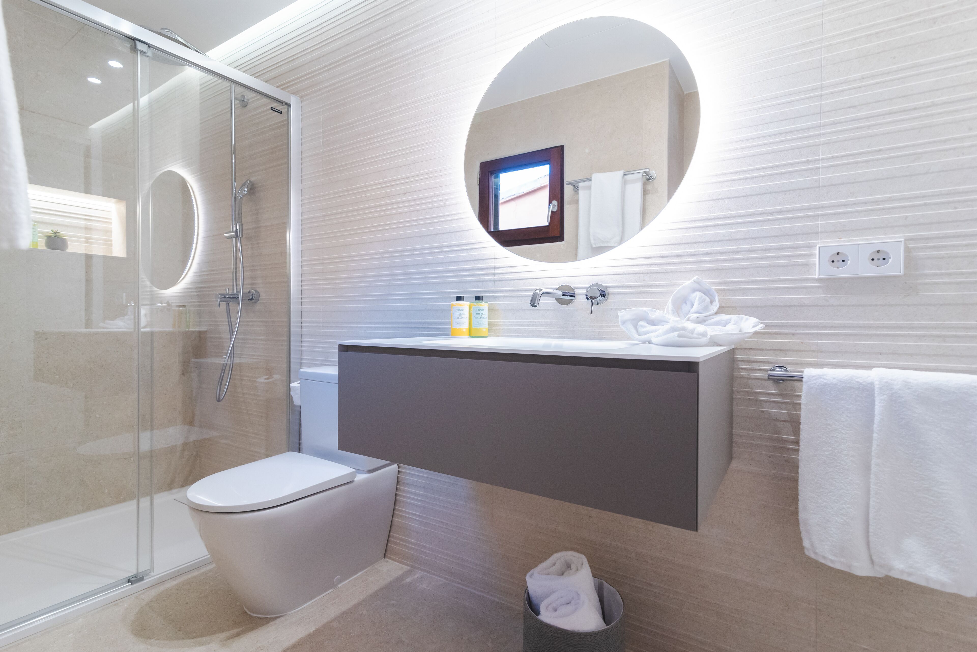 Ein modernes Badezimmer mit einer Duschkabine, einer weißen Toilette, einem Waschtisch mit Spiegel und einem Handtuchhalter.
