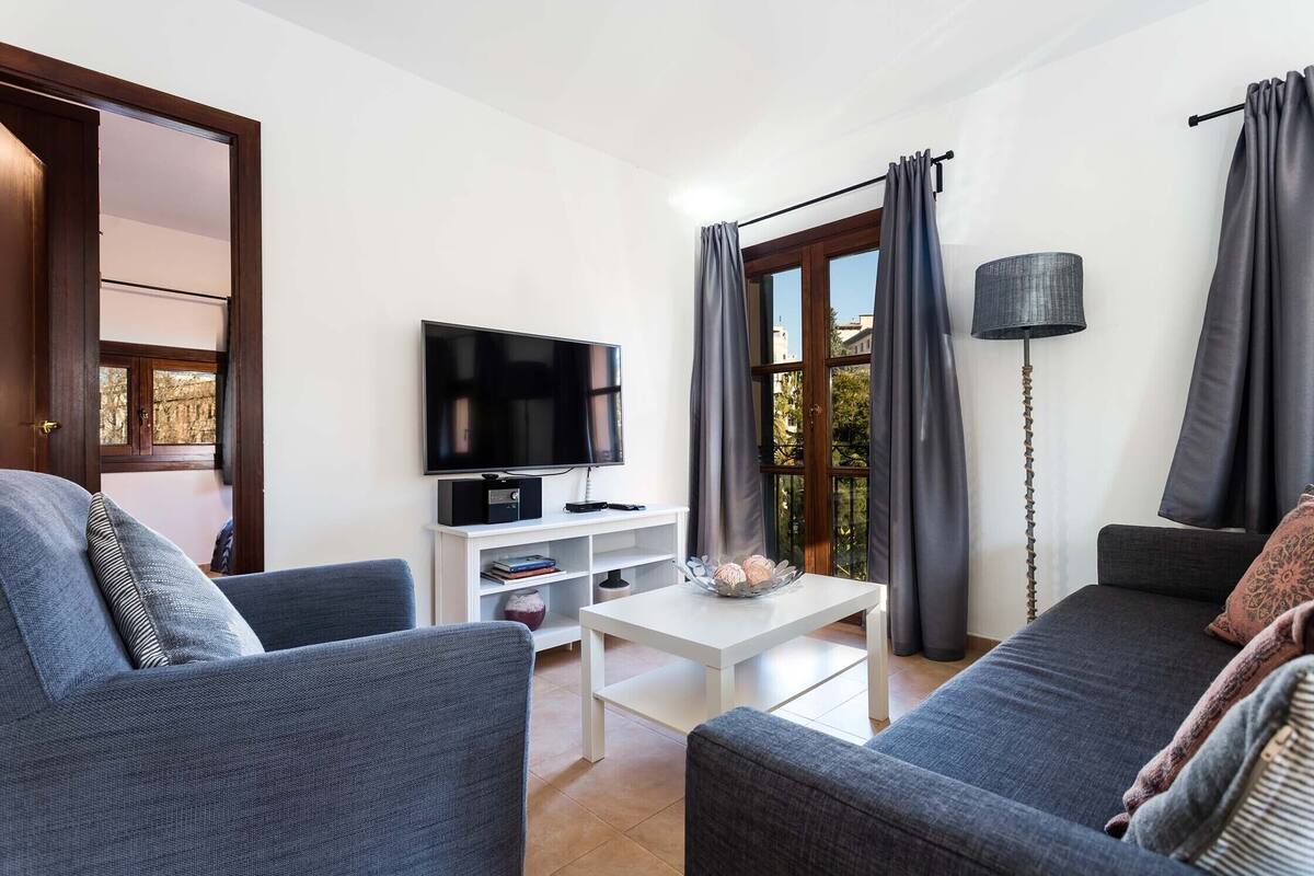 Una sala de estar moderna con un televisor de pantalla plana, sofás grises, una mesa de centro blanca y una estantería.
