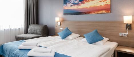 Hotelkamer met een groot bed, twee kussens, een stoel, een nachtkastje en een schilderij van een zonsondergang.