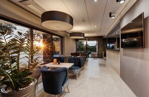 A modern restaurant with a long counter, blue upholstered chairs, and potted plants. - Wind Hotel (Kolobrzeg)