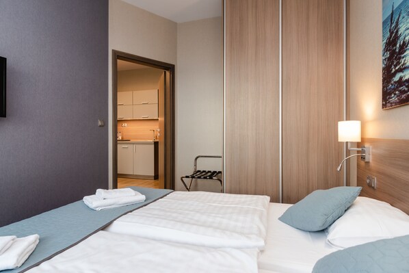A hotel room with a bed, a side table, a wall-mounted lamp, and a view of the kitchen through an open door. - Wind Hotel (Kolobrzeg)