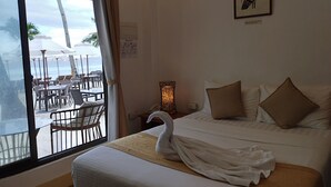 Habitación de hotel con una cama, decoración de cisne, una obra de arte enmarcada, una mesita de noche y vistas a la playa y sombrillas a través de un ventanal grande.