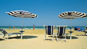 Una spiaggia con ombrelloni a righe, lettini e una vista limpida sull'oceano.