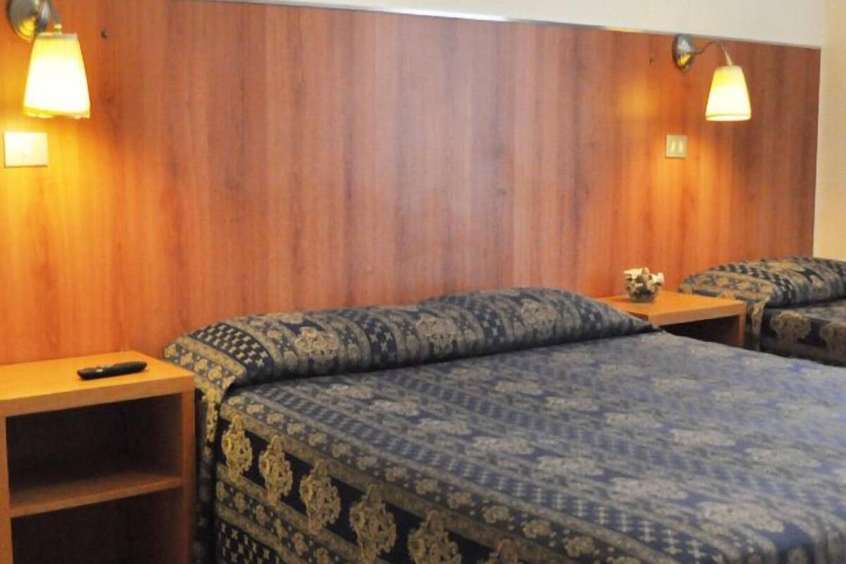 A hotel room with two beds, wooden headboard, and bedside lamps.