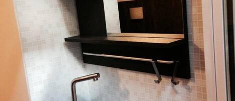 Un baño con un lavamanos blanco, repisas negras y un espejo.
