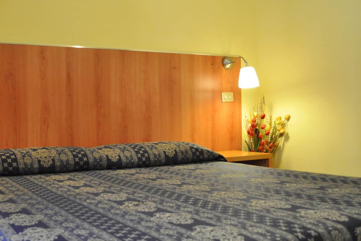 A bedroom with a wooden headboard, a patterned bedspread, bedside tables with lamps, and a vase with flowers.