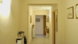 A narrow hallway with cream walls, a white door at the end, and framed pictures on the walls. - Hotel Fiorenza (Rome)