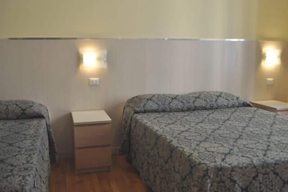 A hotel room with two beds, wooden nightstands, and wall-mounted lights.
