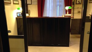 A reception area with a wooden desk, a clock on the wall, and a window with red curtains. - Hotel Fiorenza (Rome)