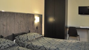 A hotel room with two beds, a desk, a chair, and a TV on the wall. - Hotel Fiorenza (Rome)