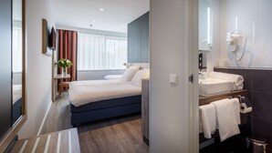 A modern hotel room with a bed, bedside table, and a bathroom with a sink and mirror. - Joy Hotel (Amsterdam)
