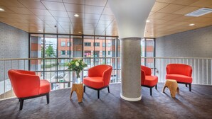 A modern lobby with red chairs, a large pillar, and a view of a building through large windows. - Joy Hotel (Amsterdam)