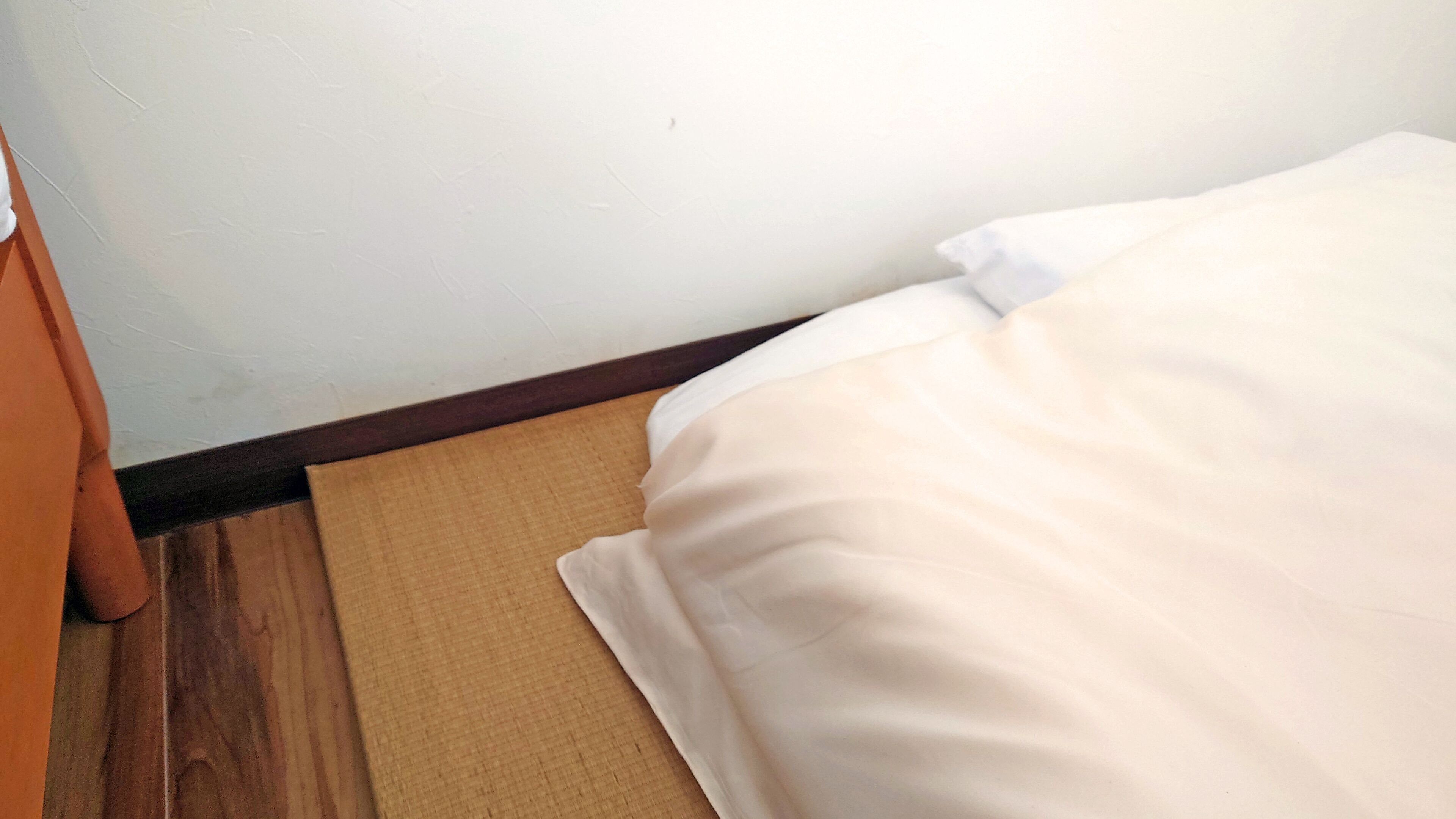 A bed with white bedding, a brown mat, and a wooden floor.