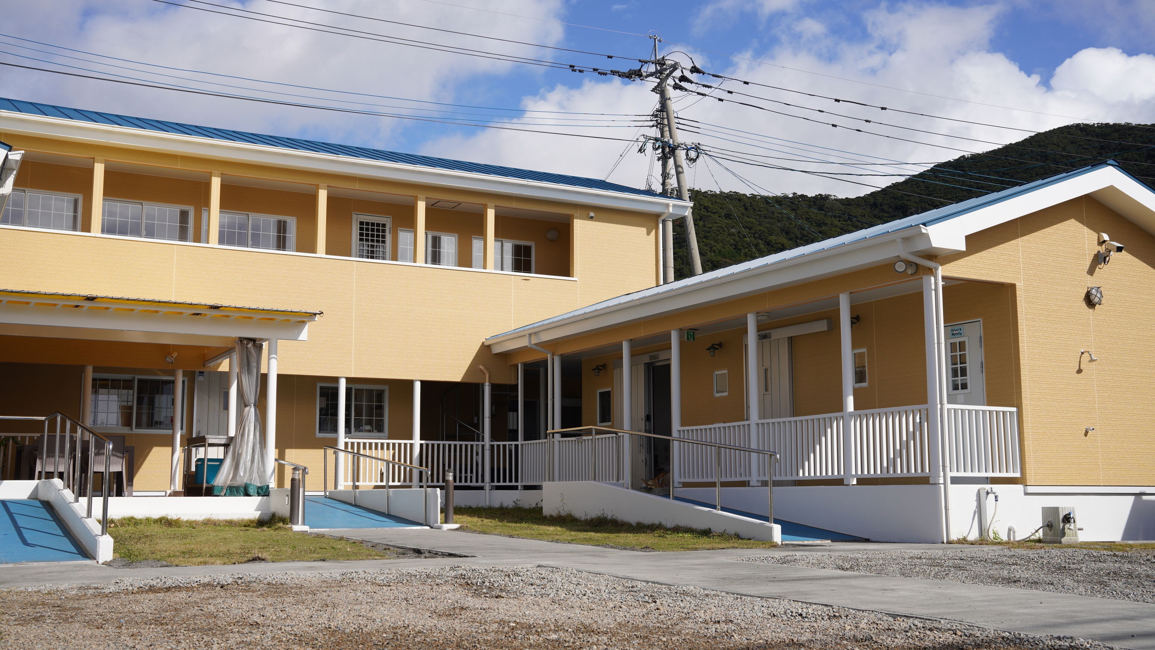 A yellow building with a blue roof, a covered entrance, and a staircase leading to a porch.