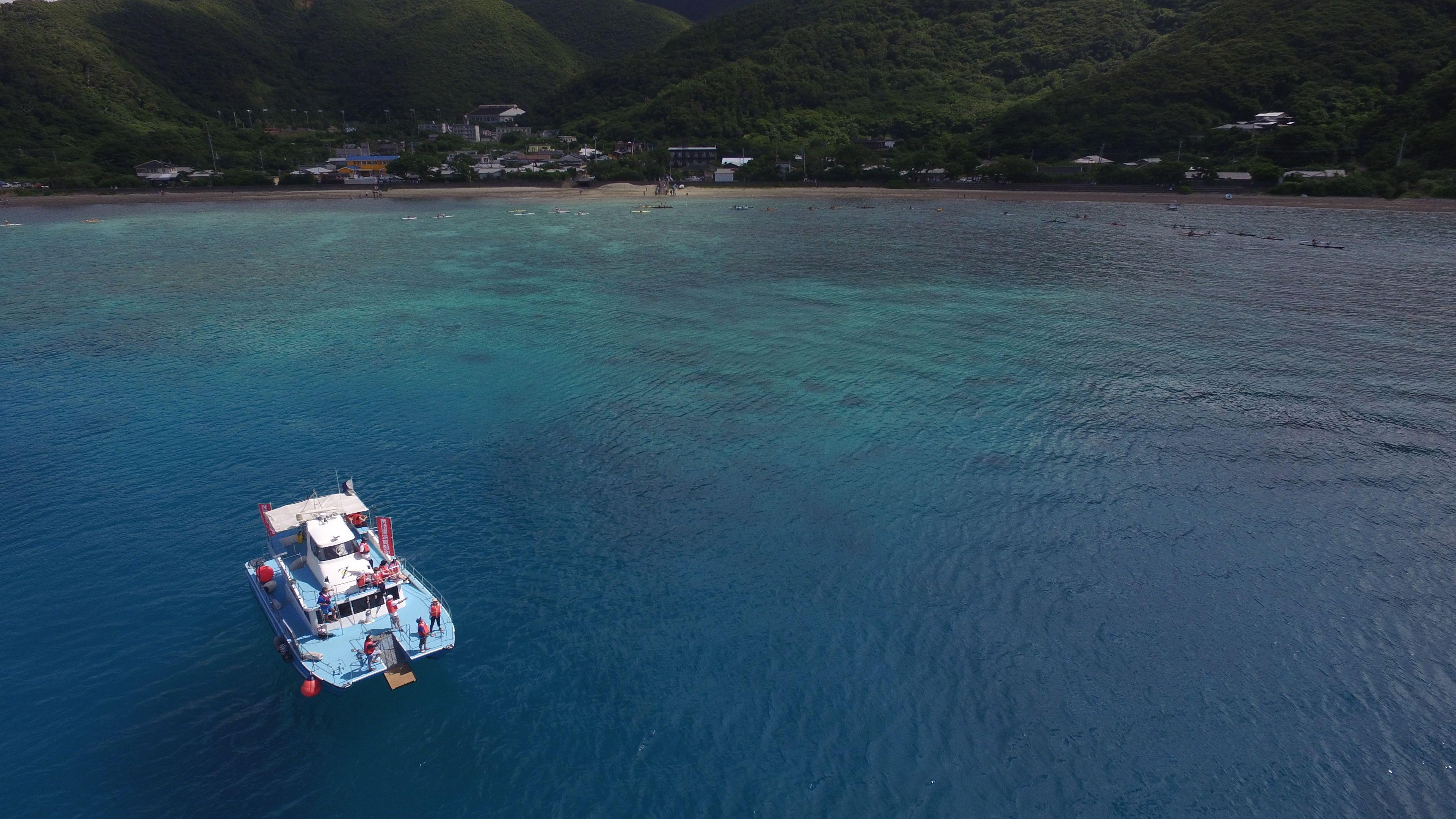 Um barco em um mar azul e límpido, com uma costa montanhosa ao fundo.