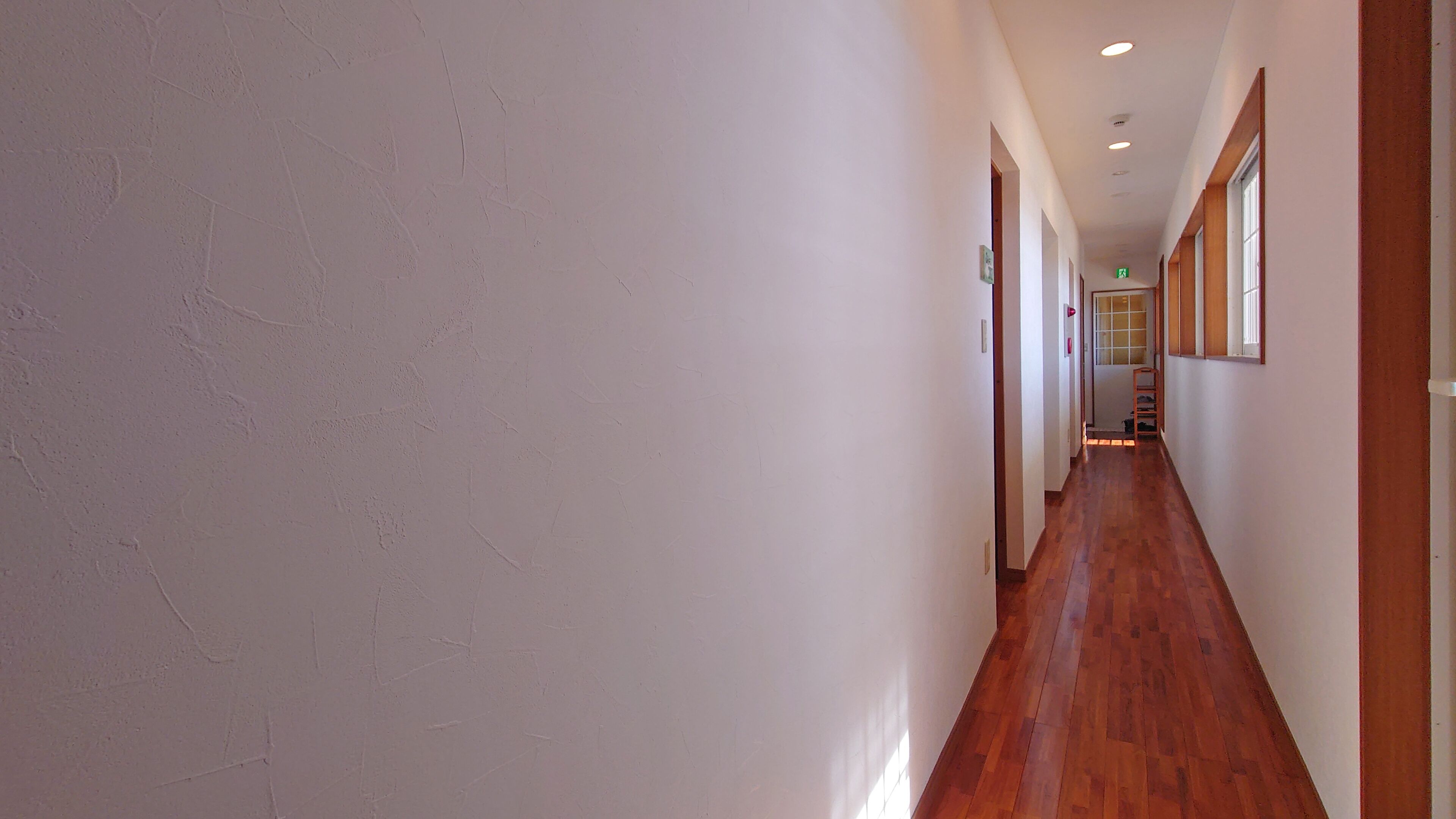 A long, narrow hallway with wooden flooring and white walls.