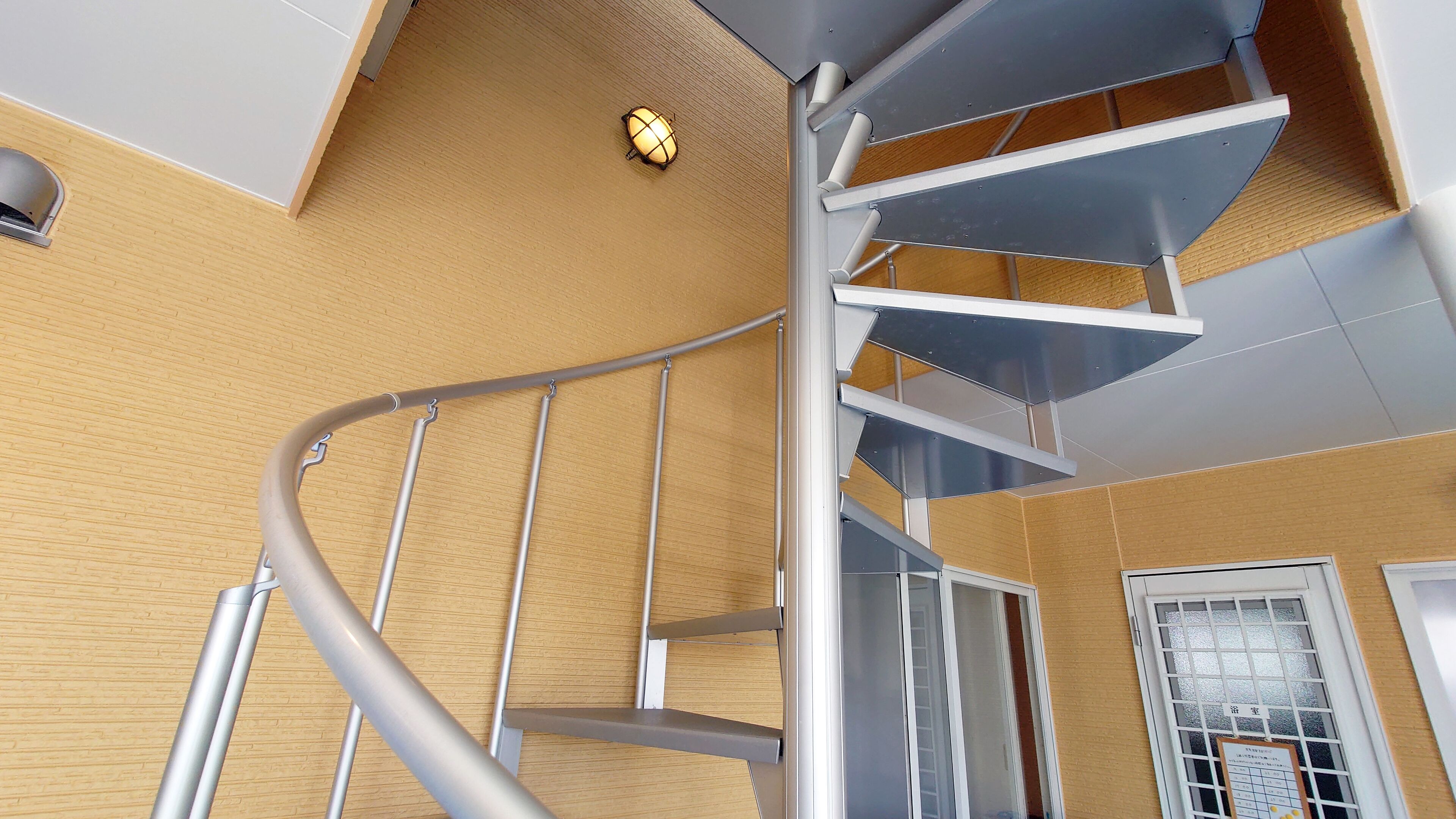 A spiral staircase with metal railings and a wooden wall.