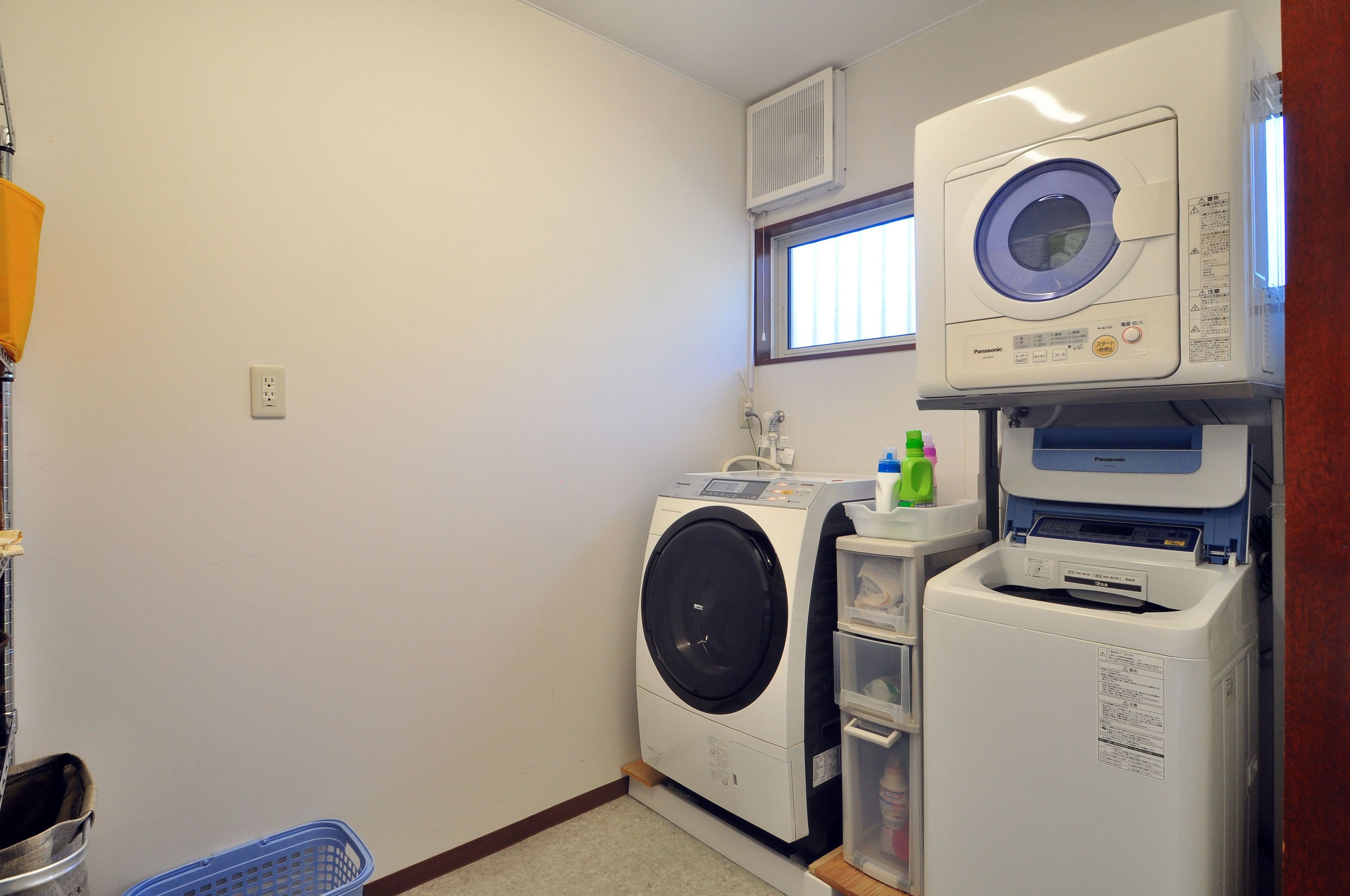 A laundry room with a front-loading washer and dryer, a small window, and a shelf with cleaning supplies.